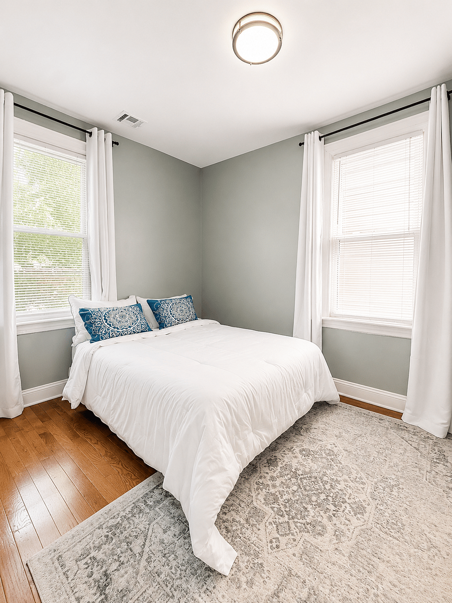 Another view of the bright bedroom with two windows and blue patterned pillows